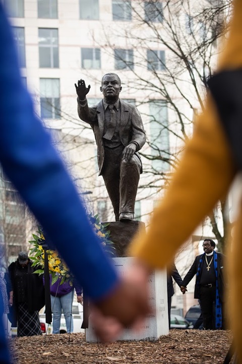 Two blurred hands are clasped in the foreground with the inscription on an MLK statue in the background the focus.