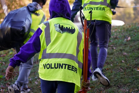 Three people wearing volunteer vests with litter cleanup tools in hand.