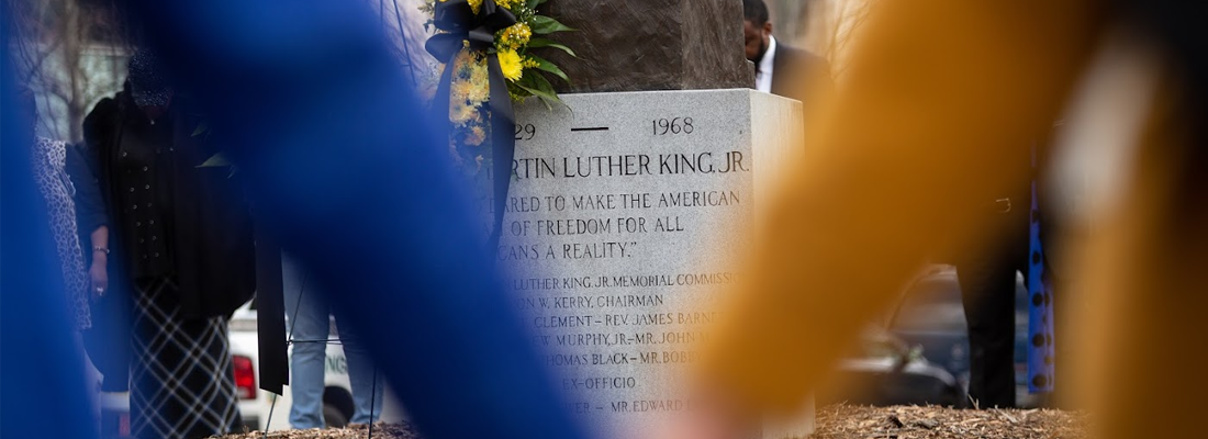 Through blurred hands held together in unity, the inscription on Martin Luther King, Jr.'s Charlotte-based statue is framed.