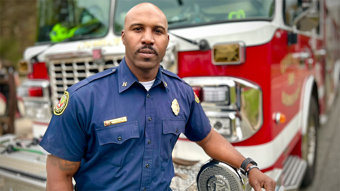 Captain Andre Fuller stands proudly in front of a Charlotte Fire engine, embodying his dedication to community service and mental health advocacy. His Crisis Intervention Team training has helped him de-escalate crises and provide lifesaving resources to those in need.