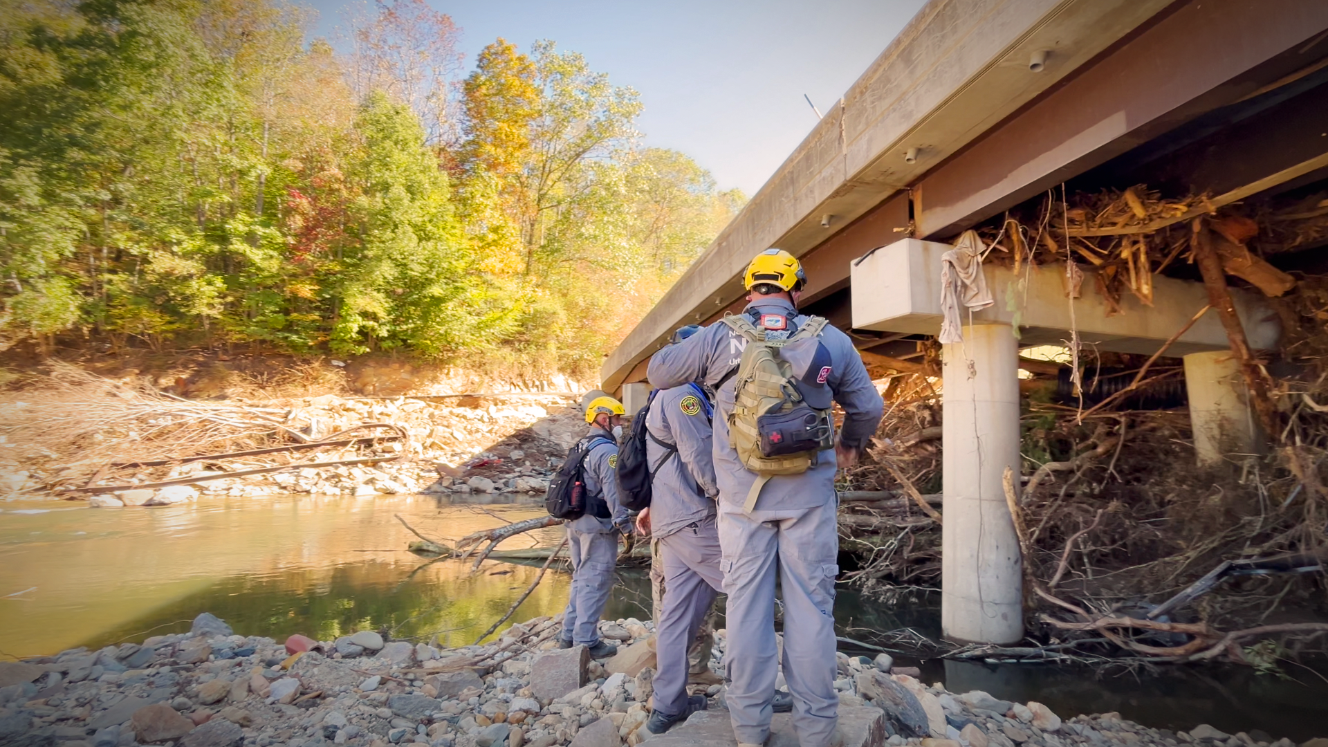 Crews pause to gather information and check coordinates, maintaining precision and focus as they search the debris under a highway bridge in Yancey County.