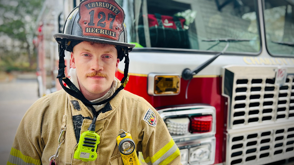 Gabriel Howard stands ready in his recruit helmet and gear, embodying the dedication required of Charlotte Fire’s newest team members. His journey to this moment includes service in both firefighting and the National Guard. 