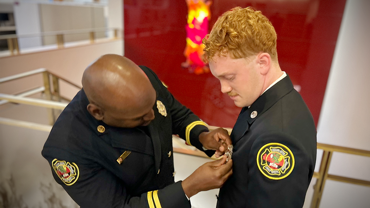 Captain Jason Cook pins Gabriel Howard with his Charlotte Fire badge in a heartfelt ceremony. The moment symbolizes Howard’s official entry into the fire department following his deployment. 