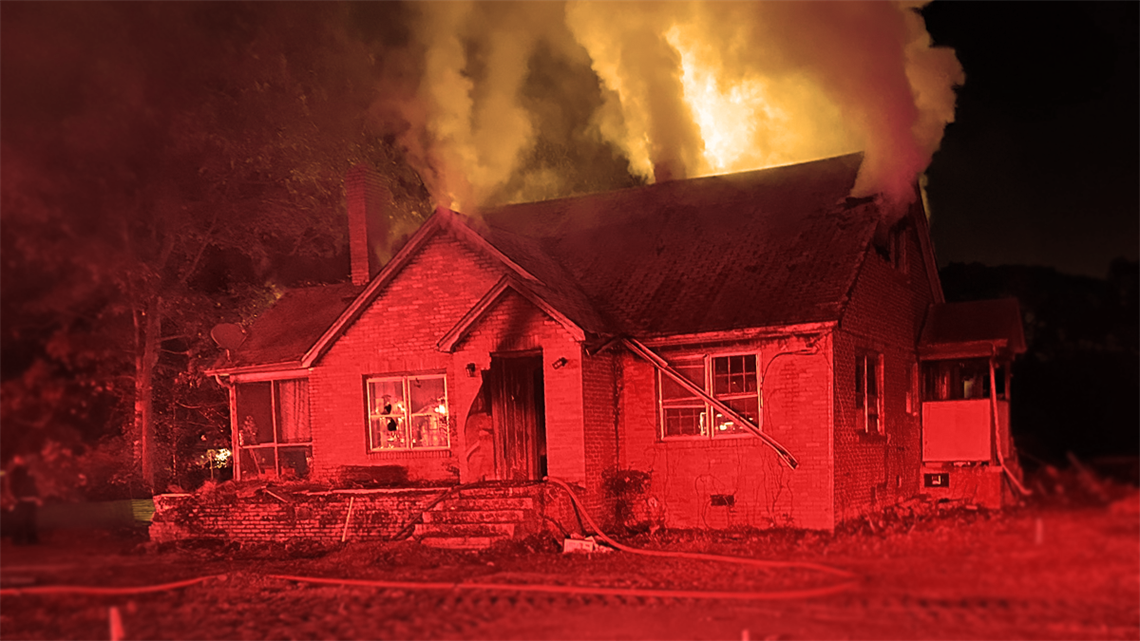 A view of the front of the residential structure with active firefighting efforts underway.