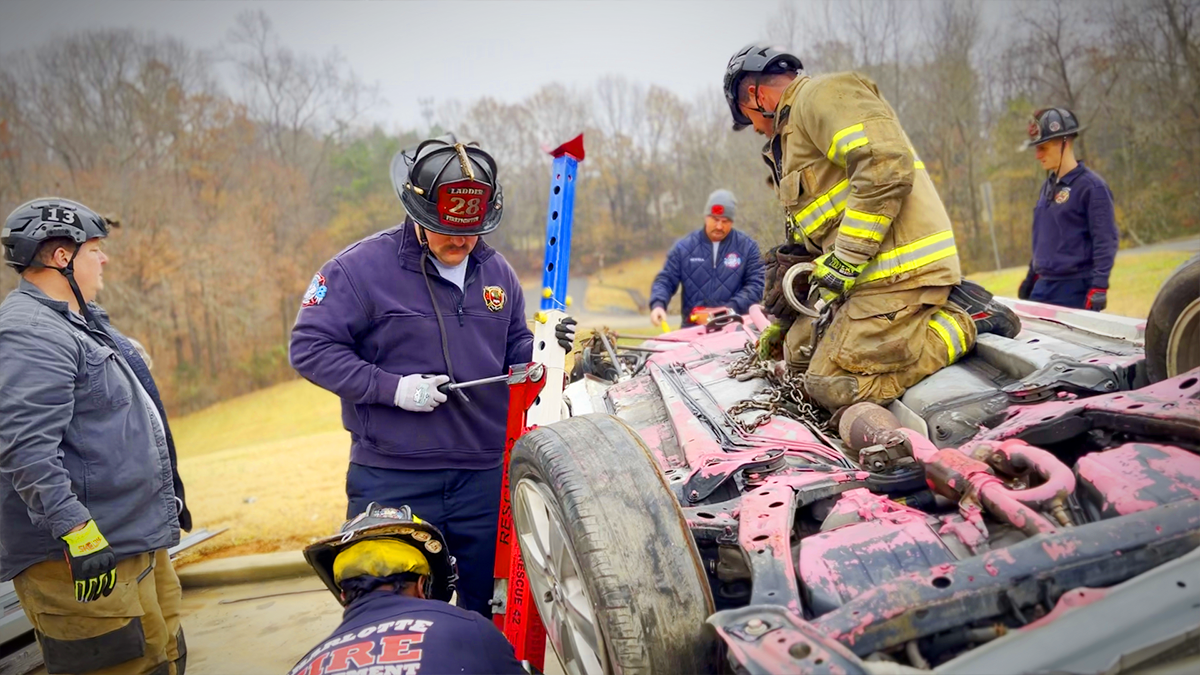 Firefighters engage in hands-on vehicle stabilization training, working together to secure an overturned car.