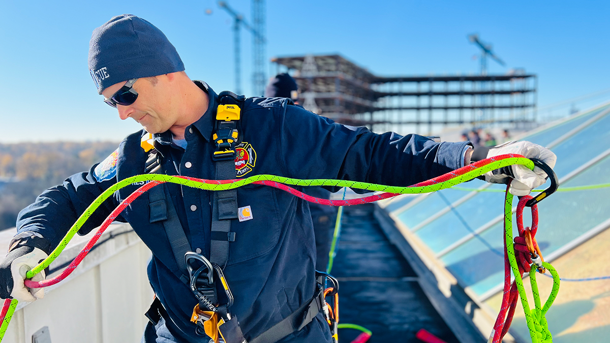 El ingeniero Brett Suhr inspecciona y prepara cuidadosamente las cuerdas de seguridad en la parte superior del Hospital de Niños Levine, asegurándose de que cada detalle sea perfecto para el evento festivo.