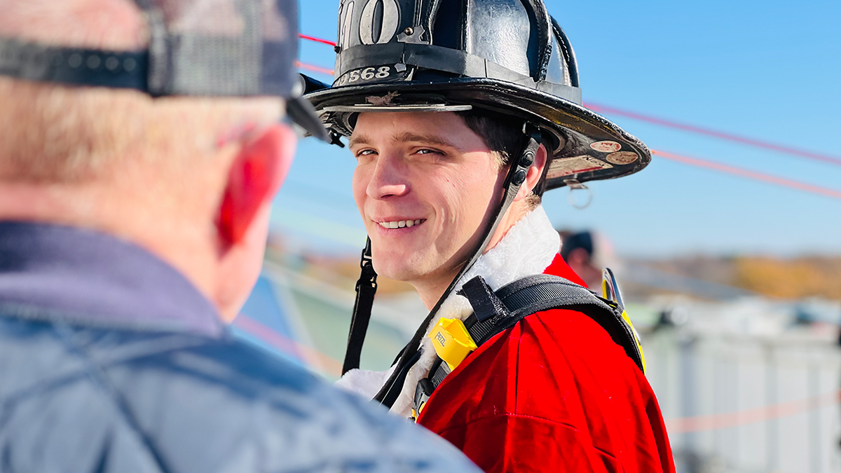 El bombero Colin Ballew sonríe antes de prepararse para el rapel, lo que refleja la alegría y la camaradería que definen esta preciada tradición.