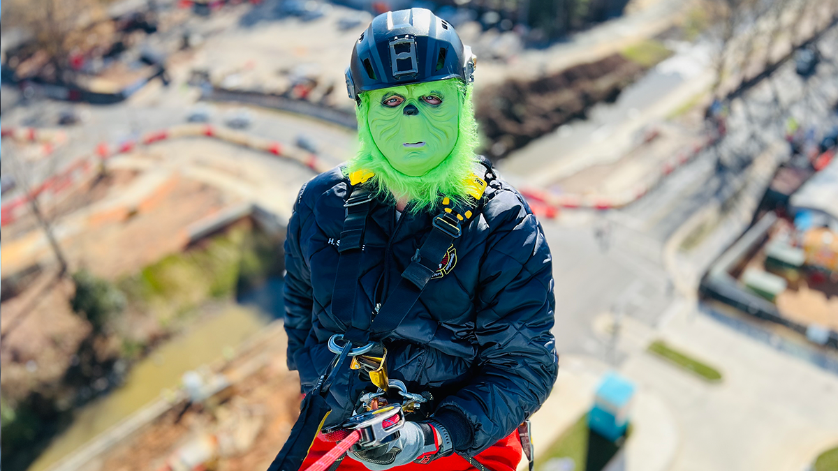 El Grinch se toma un momento durante el rapel, personificando tanto la travesura como la alegría navideña mientras ayuda a Charlotte Fire a llevar sonrisas al Levine Children's Hospital.