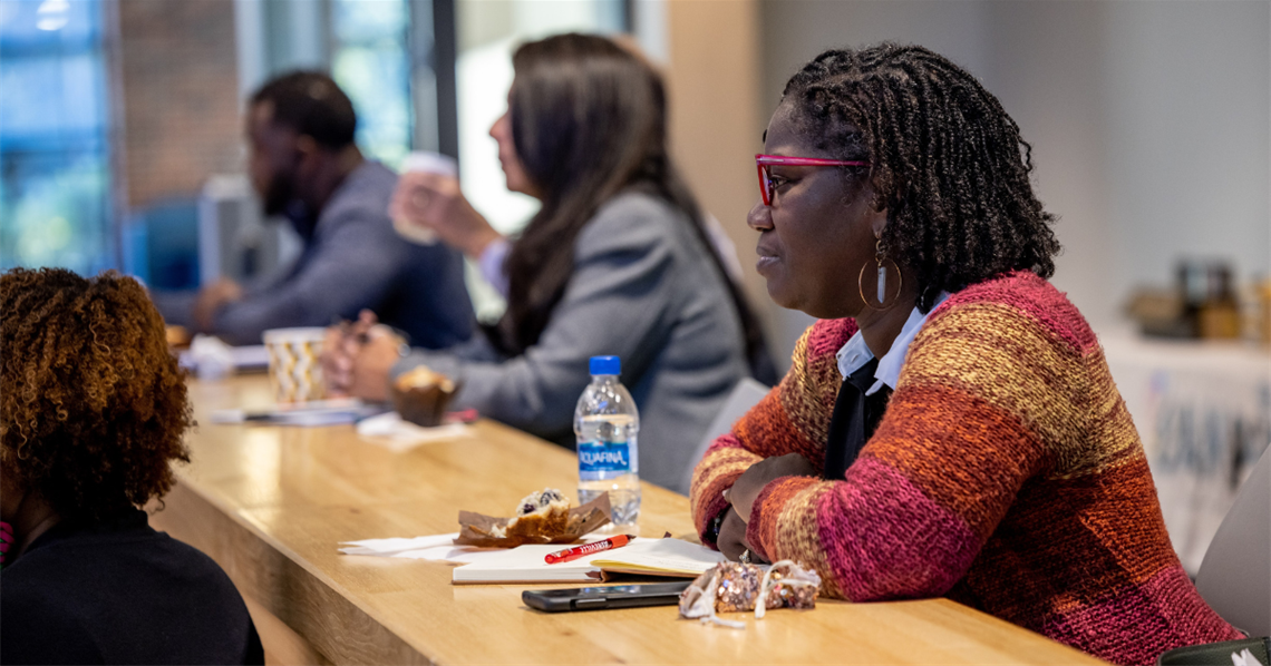 Members of a previous AMP Up cohort meet. The woman in frame listens closely during a presentation.