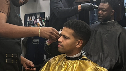 Two men in  a barber shop getting haircuts. 