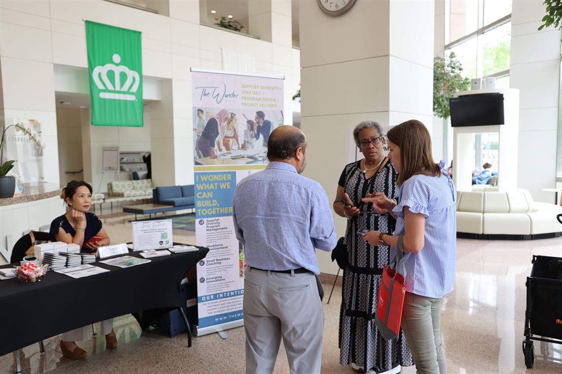 People gather during a CBI event. A group of three talk while a woman at a table looks on.