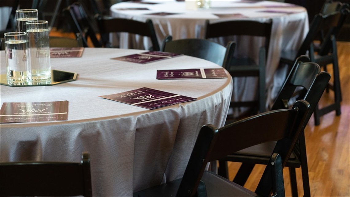 Tables are set for the 2023 Crowns of Enterprise Awards, including white linens, purple programs, and empty chairs.