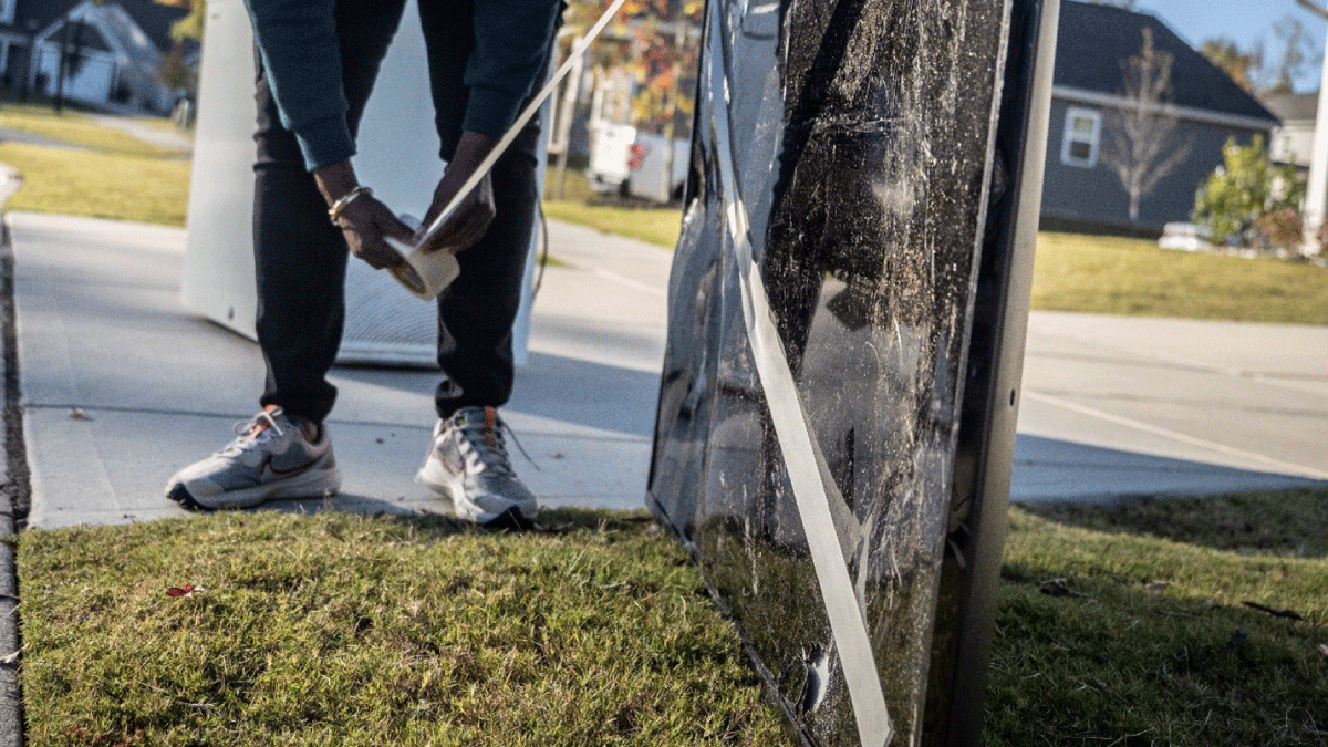 Person applying tape to the screen of a discarded television placed at the curb for collection