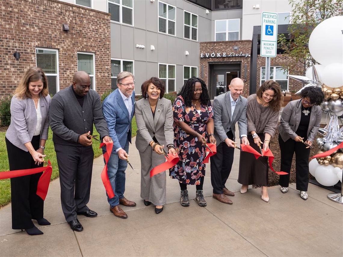 Members from Charlotte City Council, City of Charlotte staff, Crosland Southeast, and other partners smile as they cut the ribbon to officially open Evoke Living at Eastland Yards.