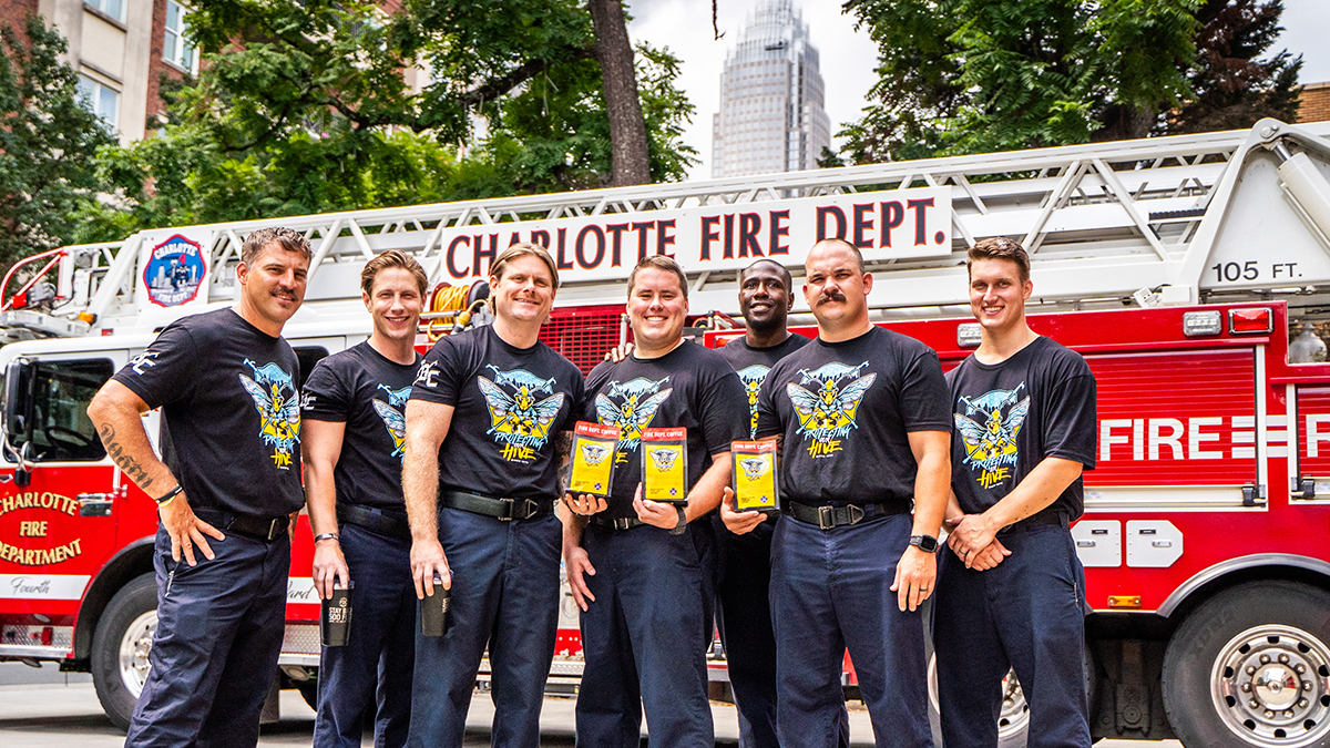 Seven Charlotte firefighters pose with their signature coffee in from of a fire engine.