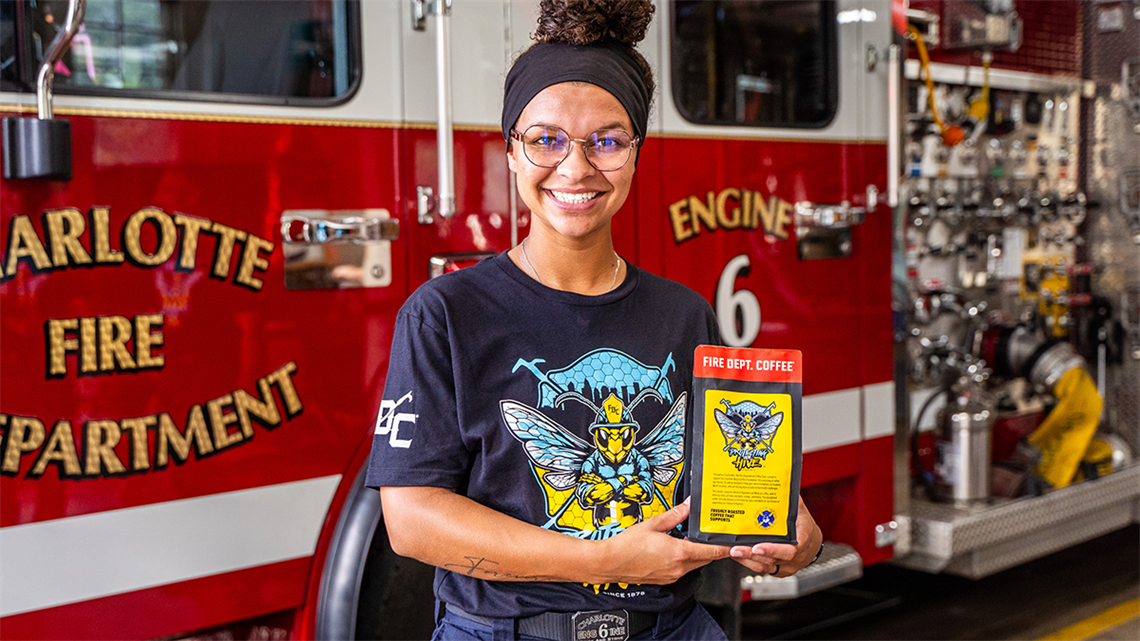 Charlotte firefighter poses in front of a fire engine holding a back of the department's new signature coffee.