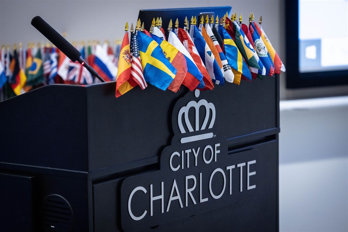 A variety of international flags appear on a black podium with the City of Charlotte logo emblazoned on the front.