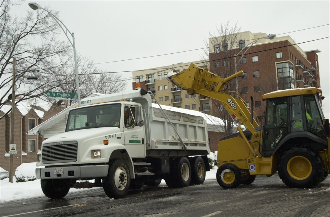 Construction equipment dumps ice and snow into a white truck that belongs to the city.