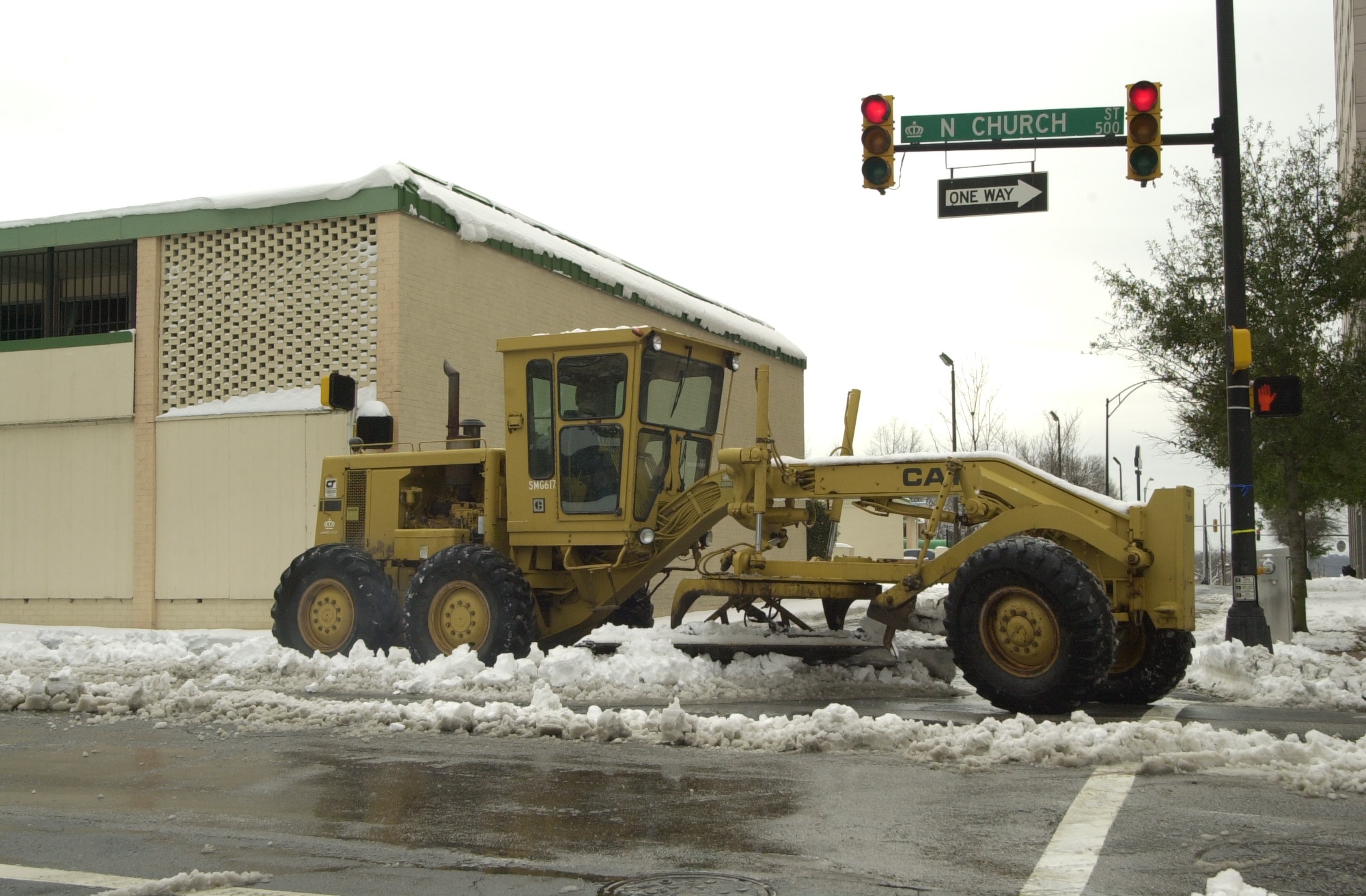 CDOT crew member clears snow and ice from the road in a large, yellow construction vehicle.