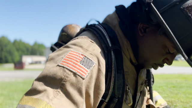 Capt. Cook prepares for training Recruiting Class 127. He leans forward, with his face in shadow. The American flag on his uniform is illuminated.