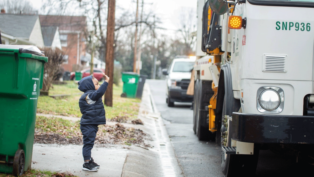 Kid standing on driveway waving at garbage truck