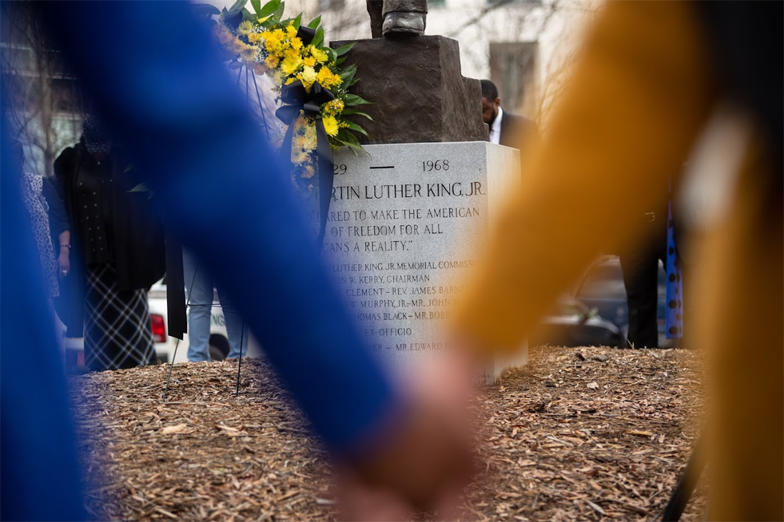 Through blurred hands held together in unity, the inscription on Martin Luther King, Jr.'s Charlotte-based statue is framed.