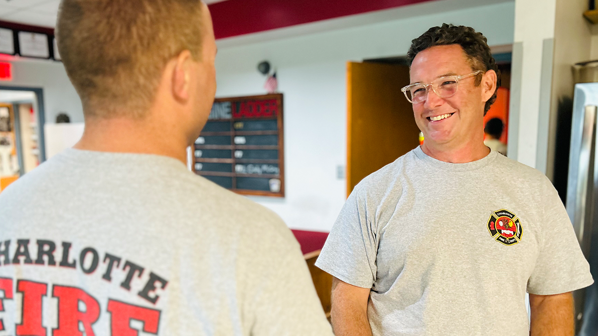 Kyle Shank smiling with a fellow firefighter in one of the Charlotte Fire stations.