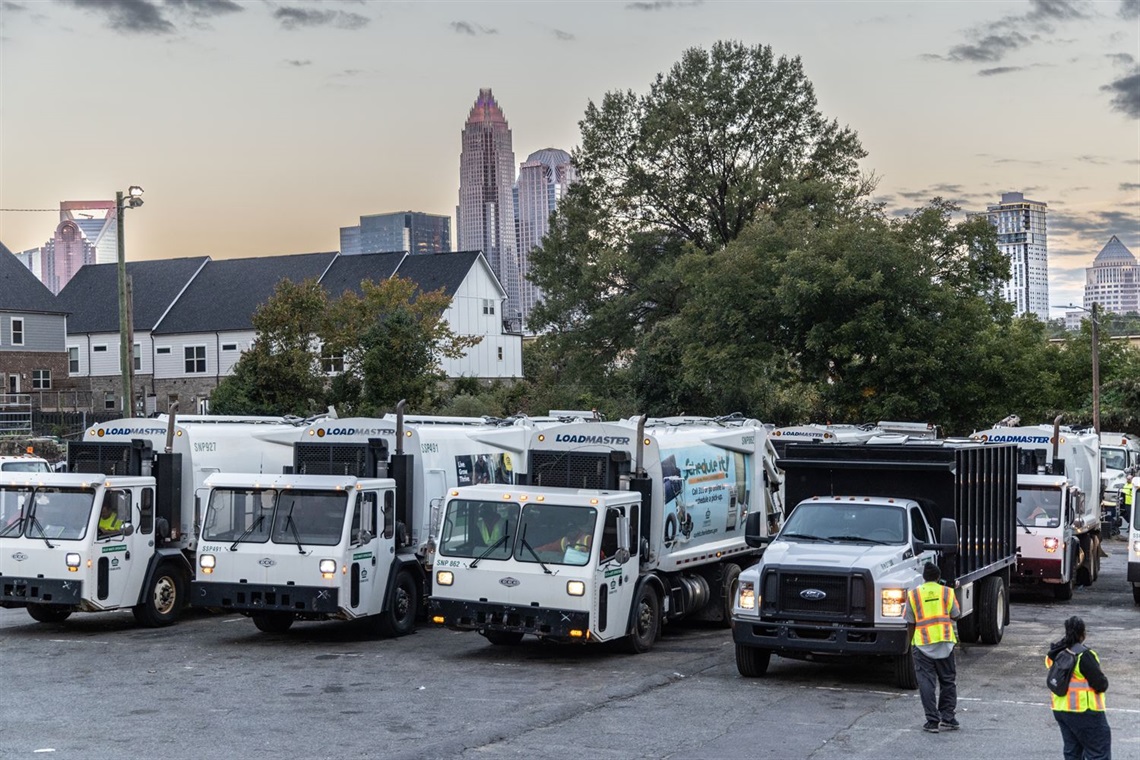 Solid Waste Services trucks prepare to leave for the morning with the Charlotte skyline behind them.