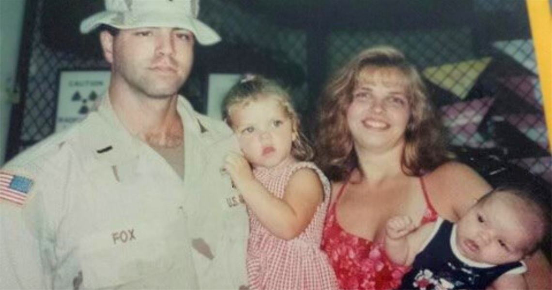 Craig Fox (left), in uniform, poses with his family. He holds one of his children while his wife holds the other.