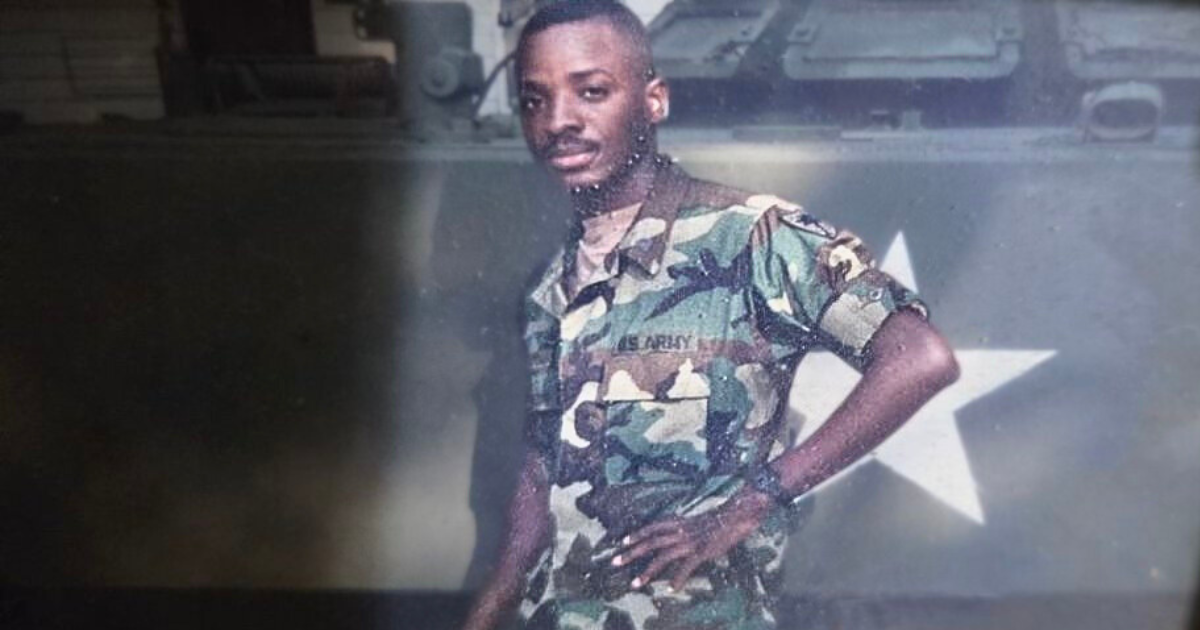 Veteran Silvester Fulmore poses in front of an Army vehicle in full combat uniform.