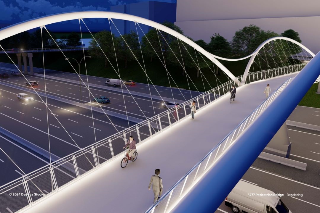 An overhead view of the Rail Trail Bridge at night showing on bicyclist and several pedestrians traveling over it