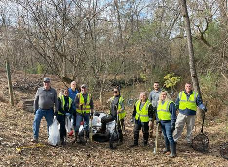 Volunteers standing along a creek they just cleaned, holding trash bags.